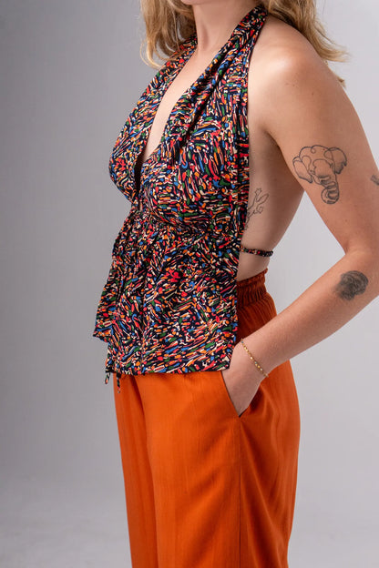 Woman wearing a colorful top and orange pants against a gray background