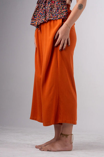 Person wearing orange pants and a patterned top on a plain background