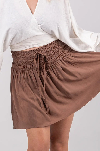 Woman wearing a white top and brown skirt on a plain background