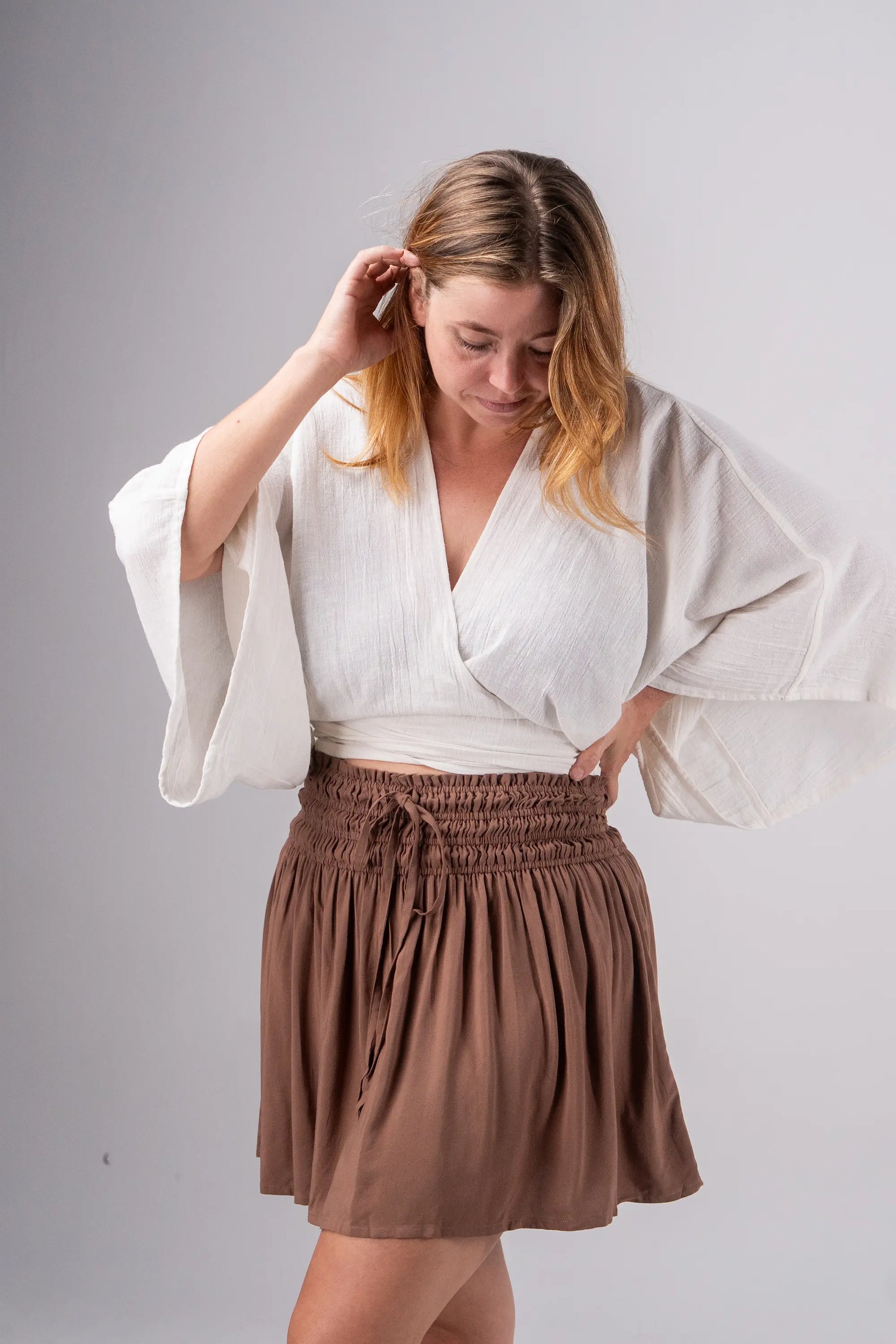 Woman wearing a white blouse and brown skirt against a gray background