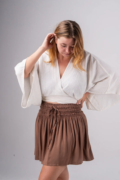 Woman wearing a white blouse and brown skirt against a gray background