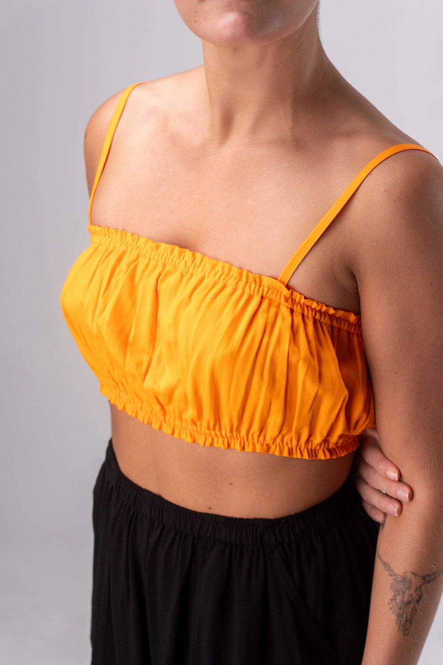 Person wearing a bright orange top with thin straps on a plain background