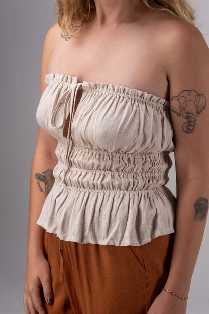 Woman wearing a beige off-shoulder top and brown pants against a gray background