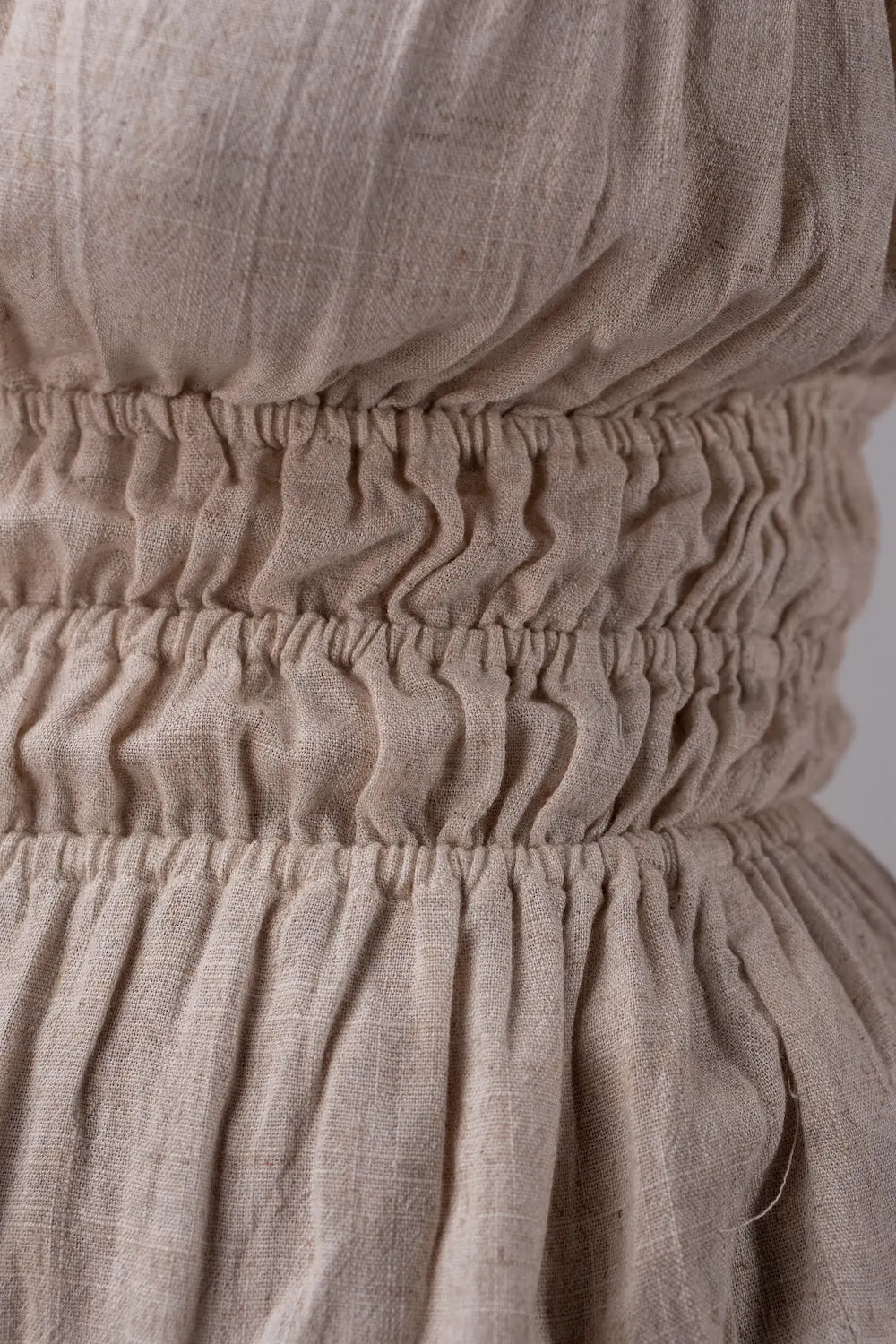 Close-up of beige fabric with a gathered waistband on a plain background