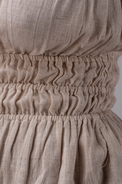 Close-up of beige fabric with a gathered waistband on a plain background