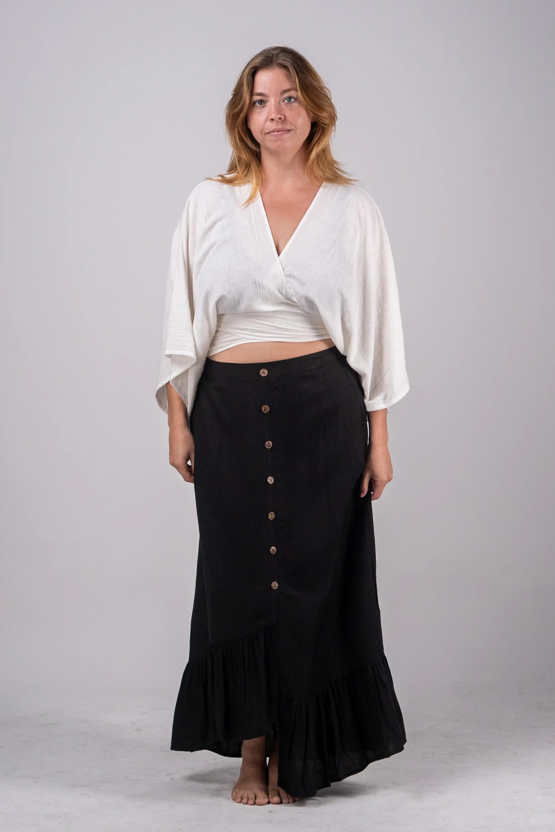 Woman wearing a white top and black skirt with buttons on a plain background