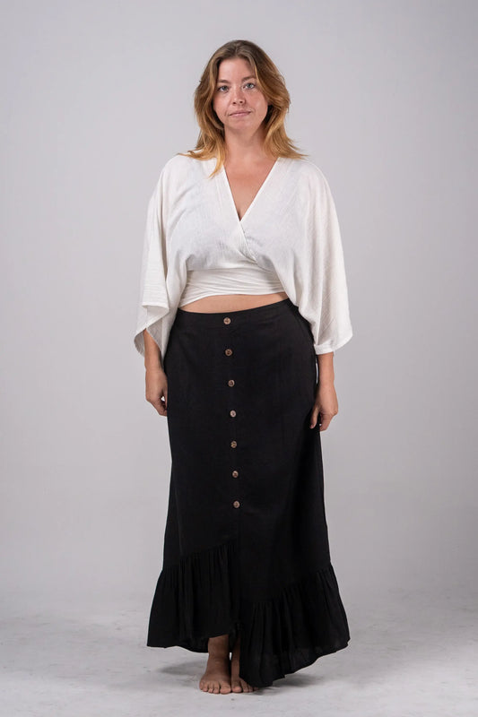 Woman wearing a white top and black skirt with buttons on a plain background