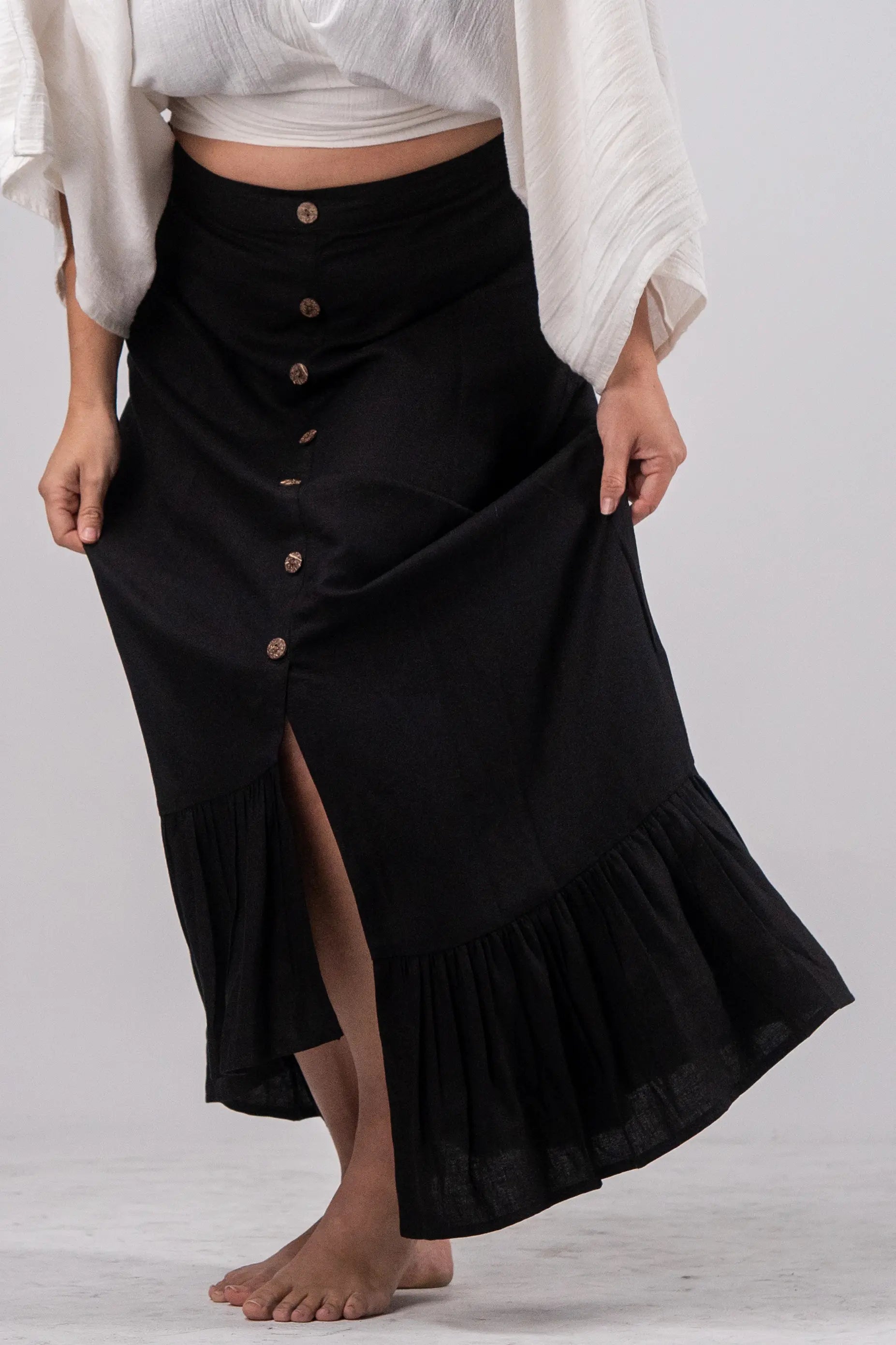 Person wearing a black skirt with buttons and a white top on a light gray background