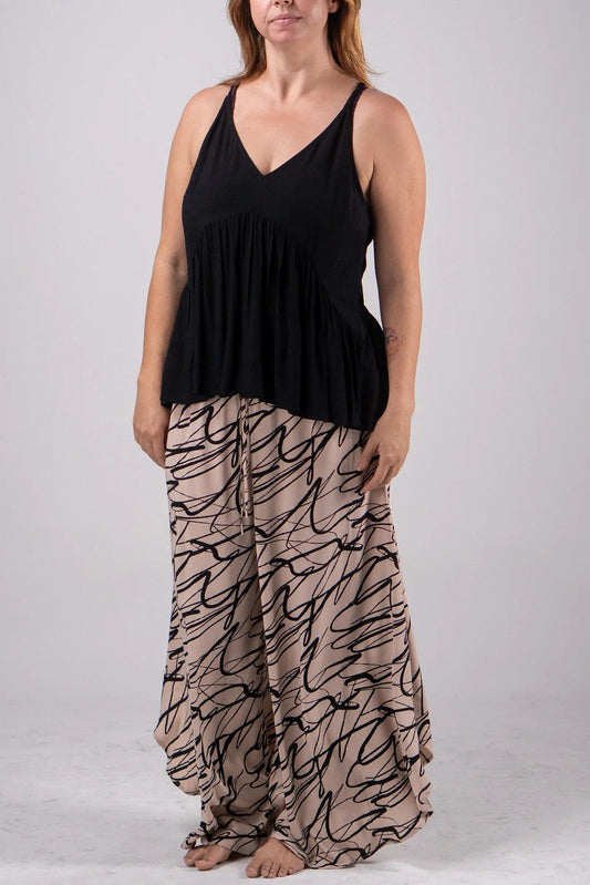 Woman wearing a black sleeveless top and patterned beige pants on a gray background