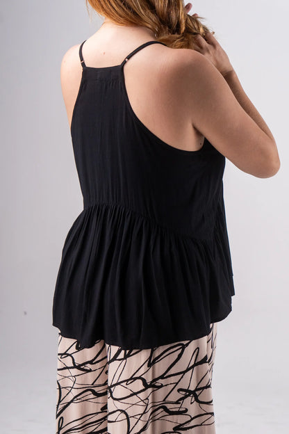 Person wearing a black sleeveless top and patterned pants on a plain background