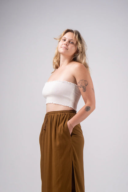 Woman wearing a white top and brown pants against a plain background