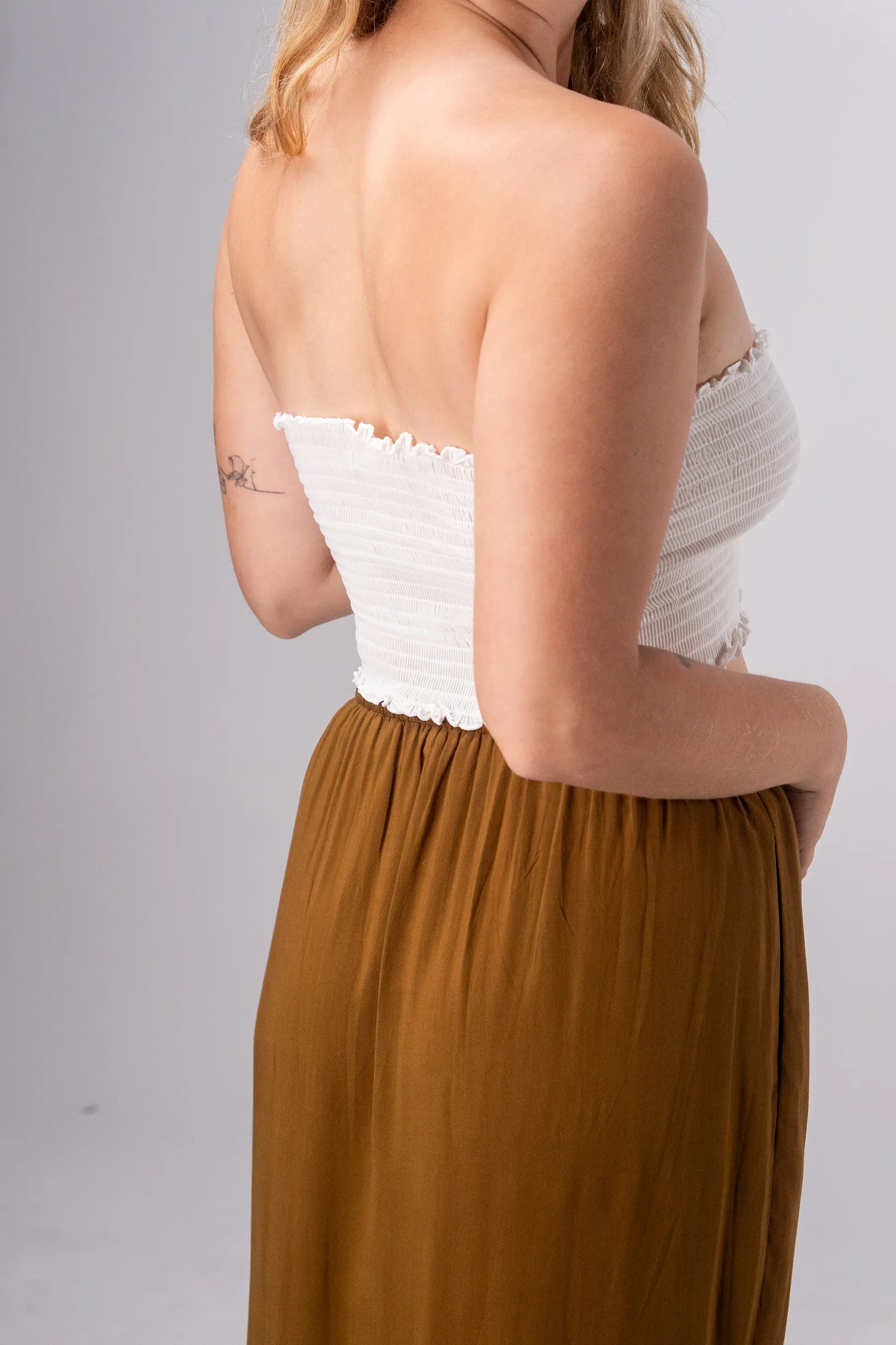 Woman wearing a white strapless top and brown skirt against a gray background