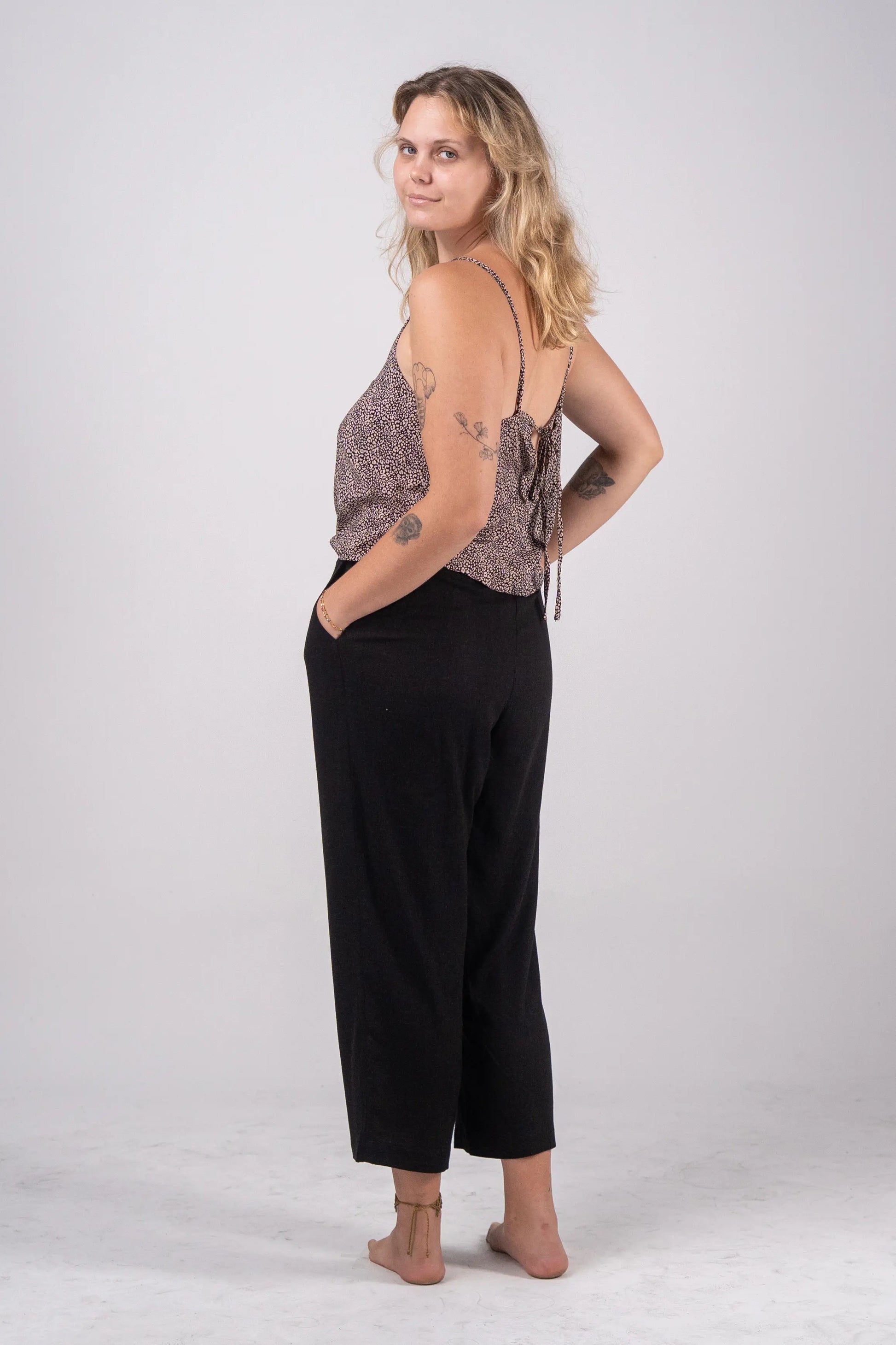 Woman wearing a patterned top and black pants on a white background