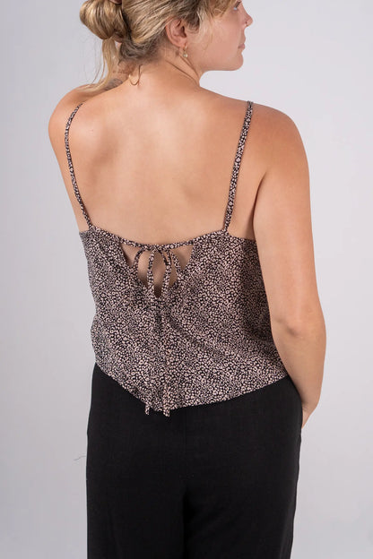 Woman wearing a patterned top with thin straps on a plain background