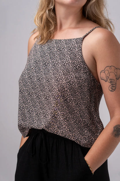 Woman wearing a patterned top and black pants against a gray background