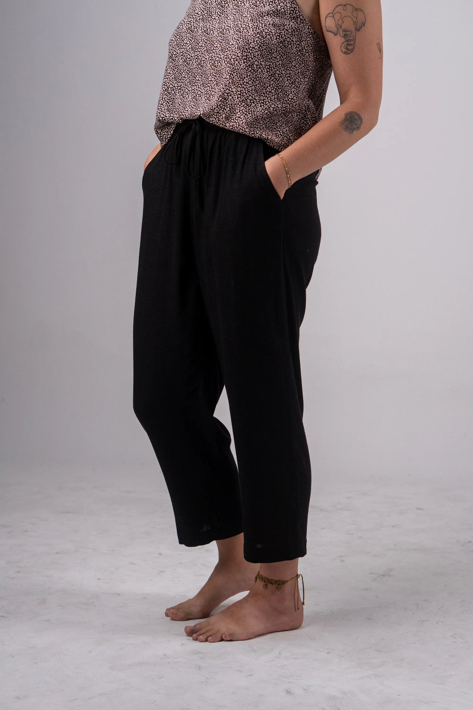 Person wearing black pants and a patterned top on a plain background