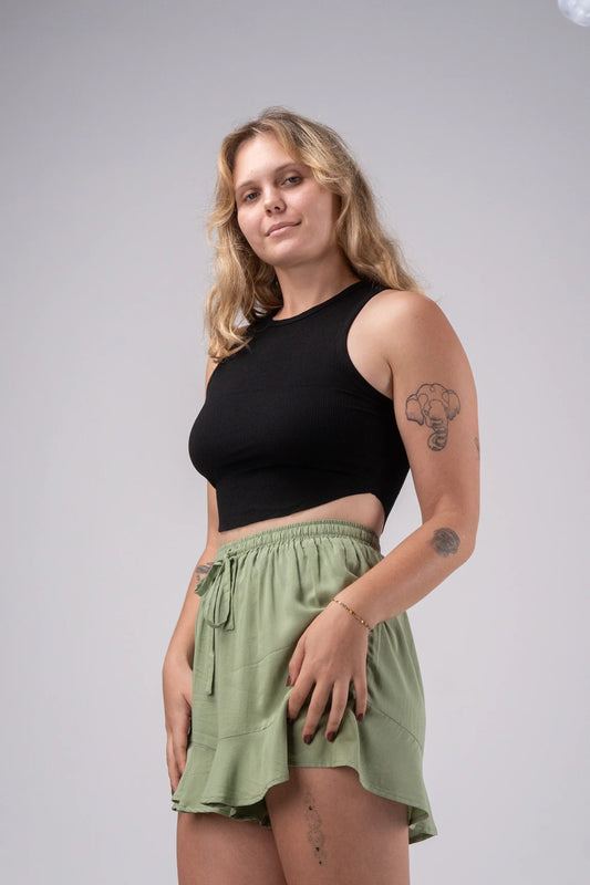 Woman wearing a black crop top and green shorts against a plain background