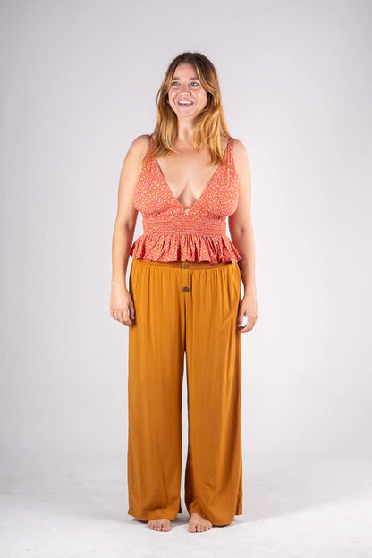 Woman wearing a red patterned top and mustard yellow pants on a white background