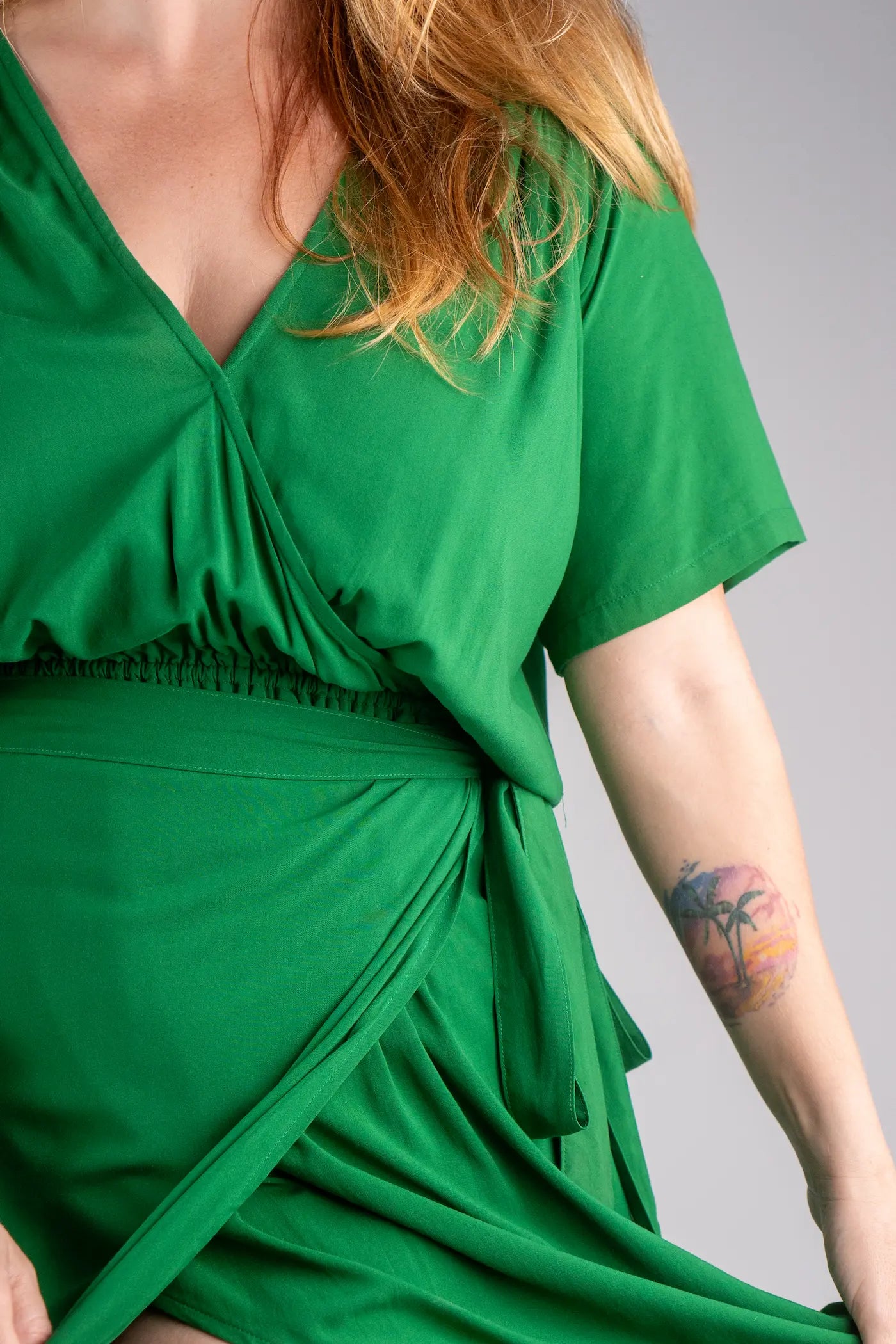 Green dress worn by a person with a tattoo on their arm against a gray background