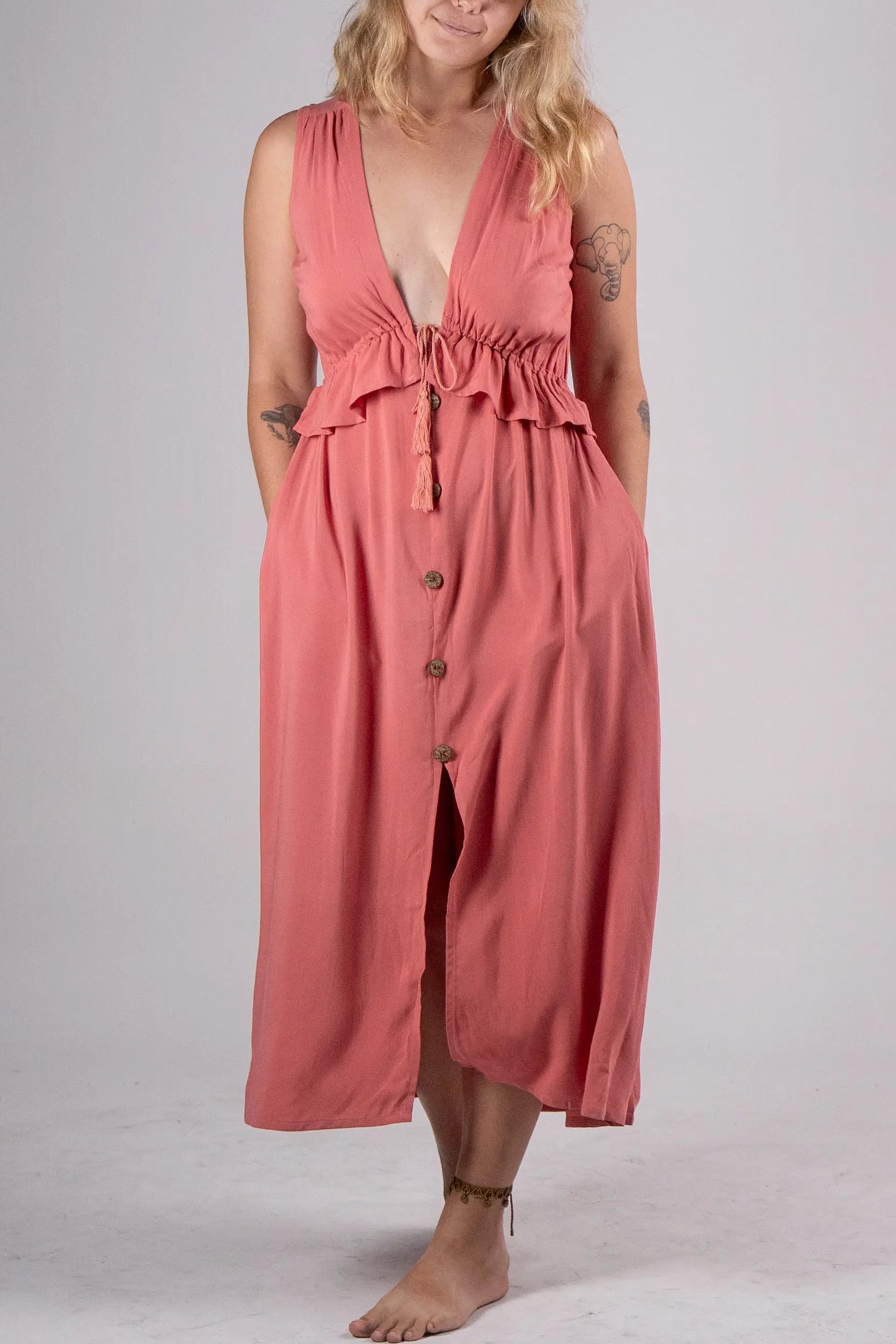 Woman wearing a coral pink dress with buttons on a plain background