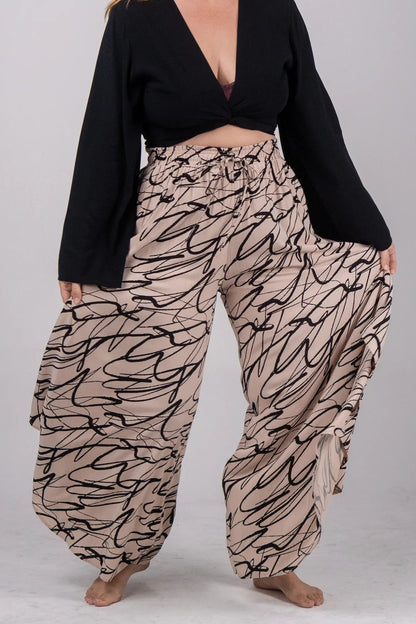 Woman wearing a black top and patterned beige pants on a gray background