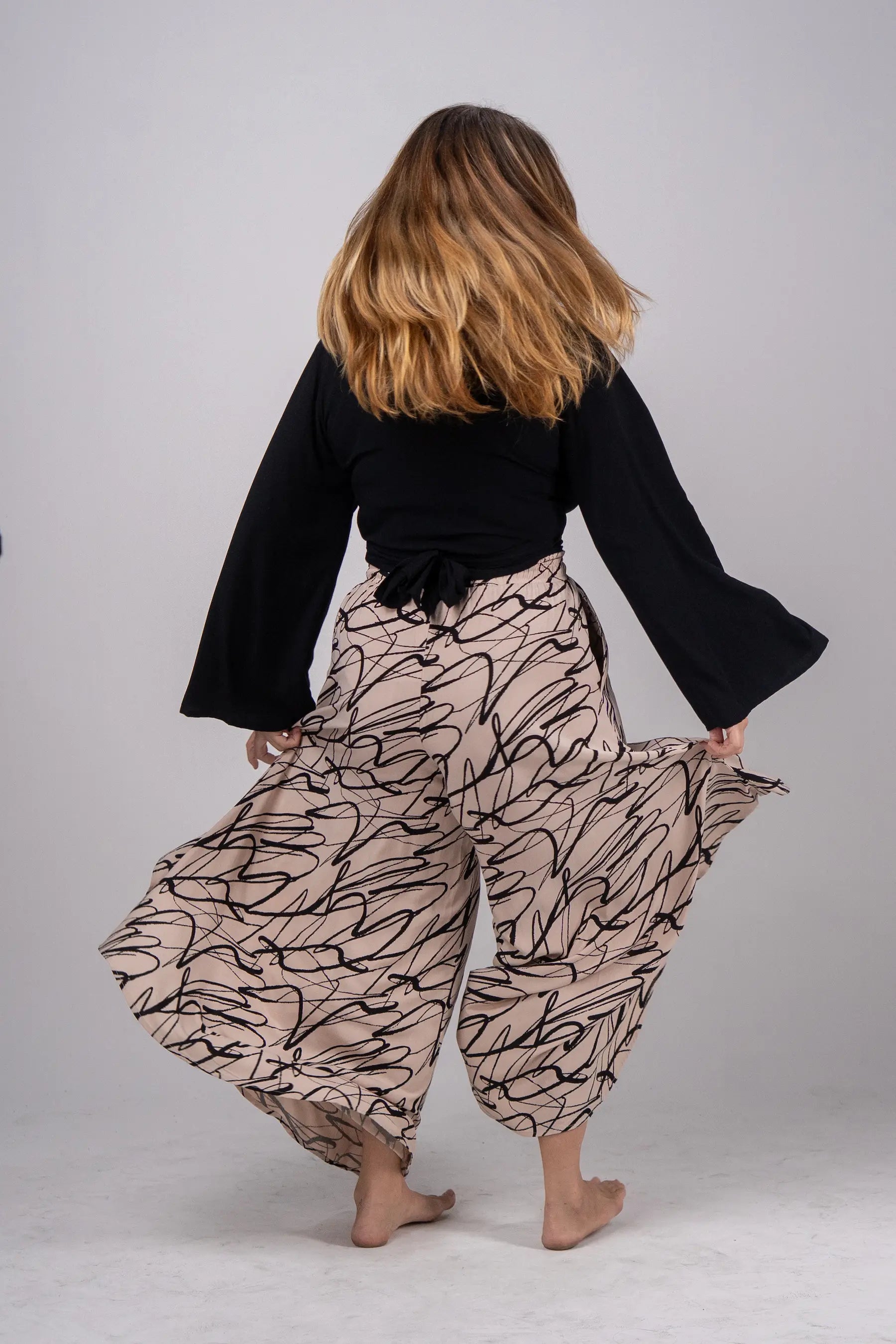 Person wearing a black top and patterned pants on a plain background