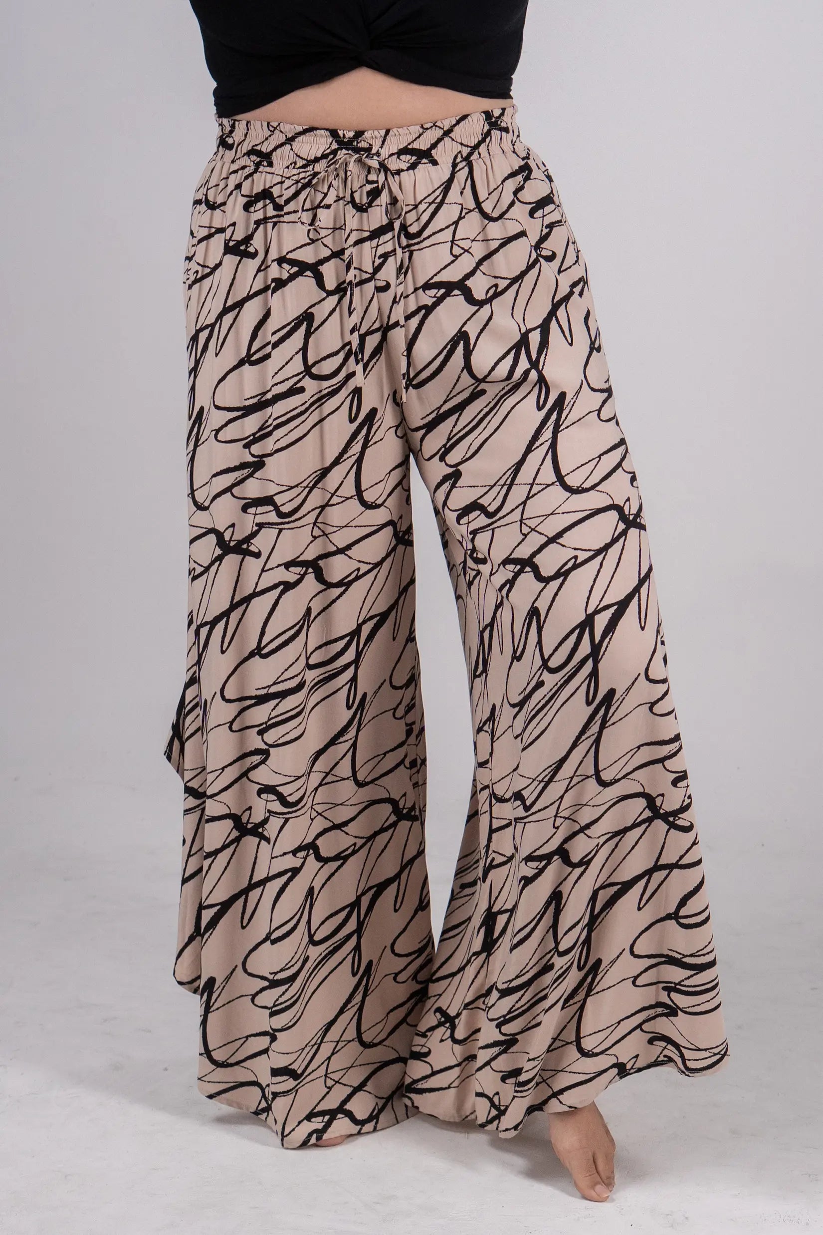 Beige wide-leg pants with black abstract pattern worn by a person on a light gray background