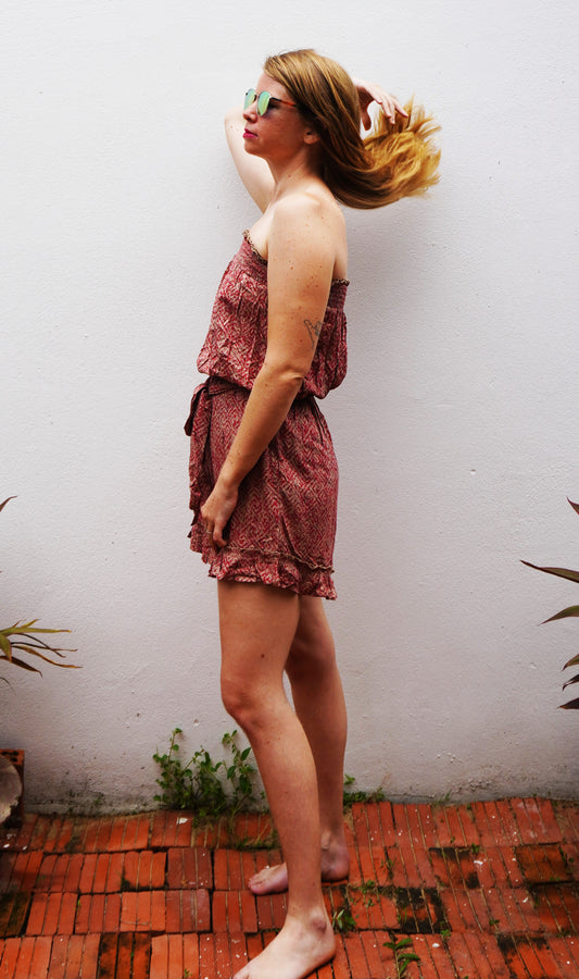 Woman in a floral dress standing against a white wall with red brick floor.