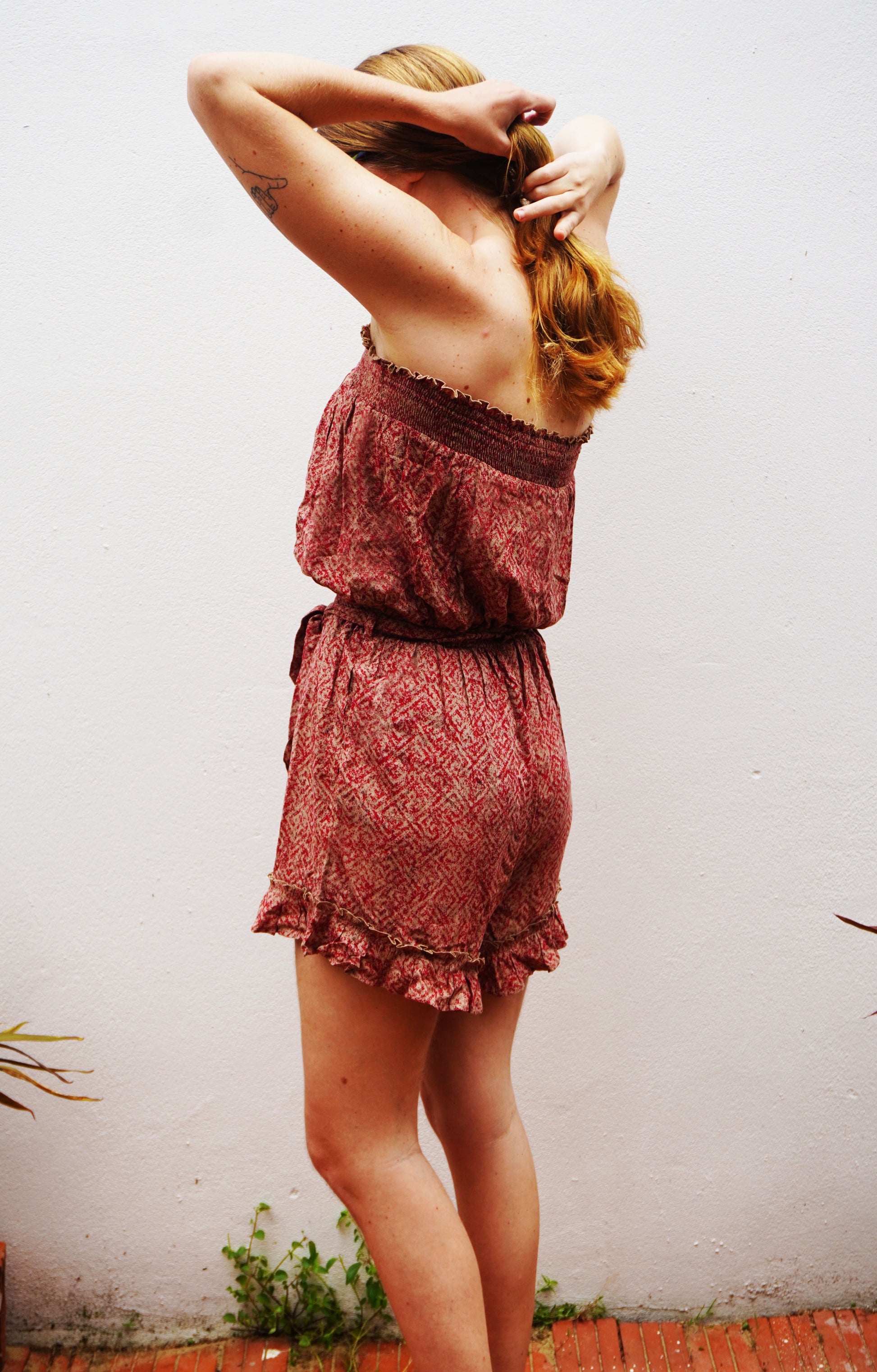 Woman wearing a patterned romper against a plain wall.