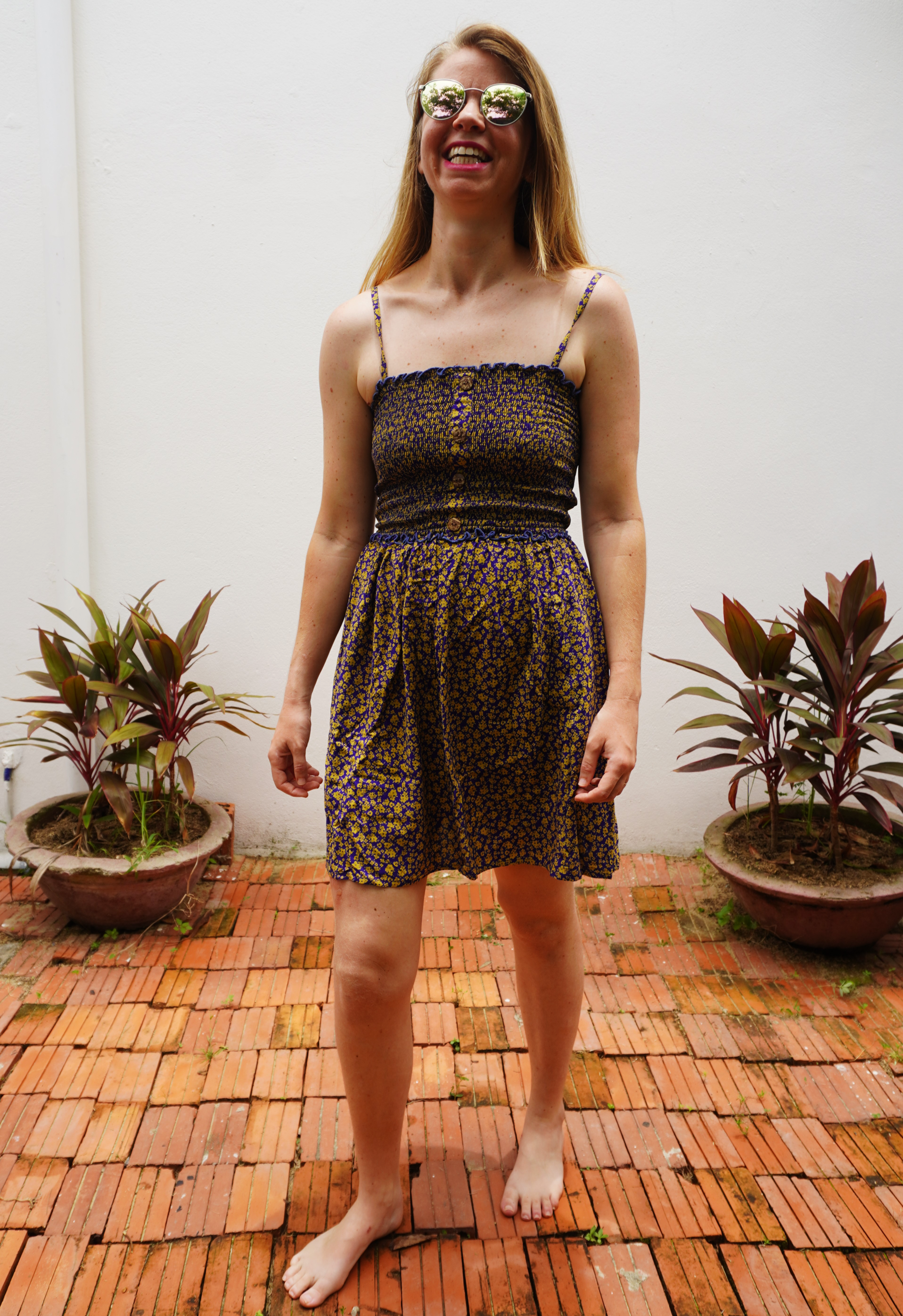 Woman wearing a purple and yellow floral patterned dress standing on a wooden floor with plants in the background