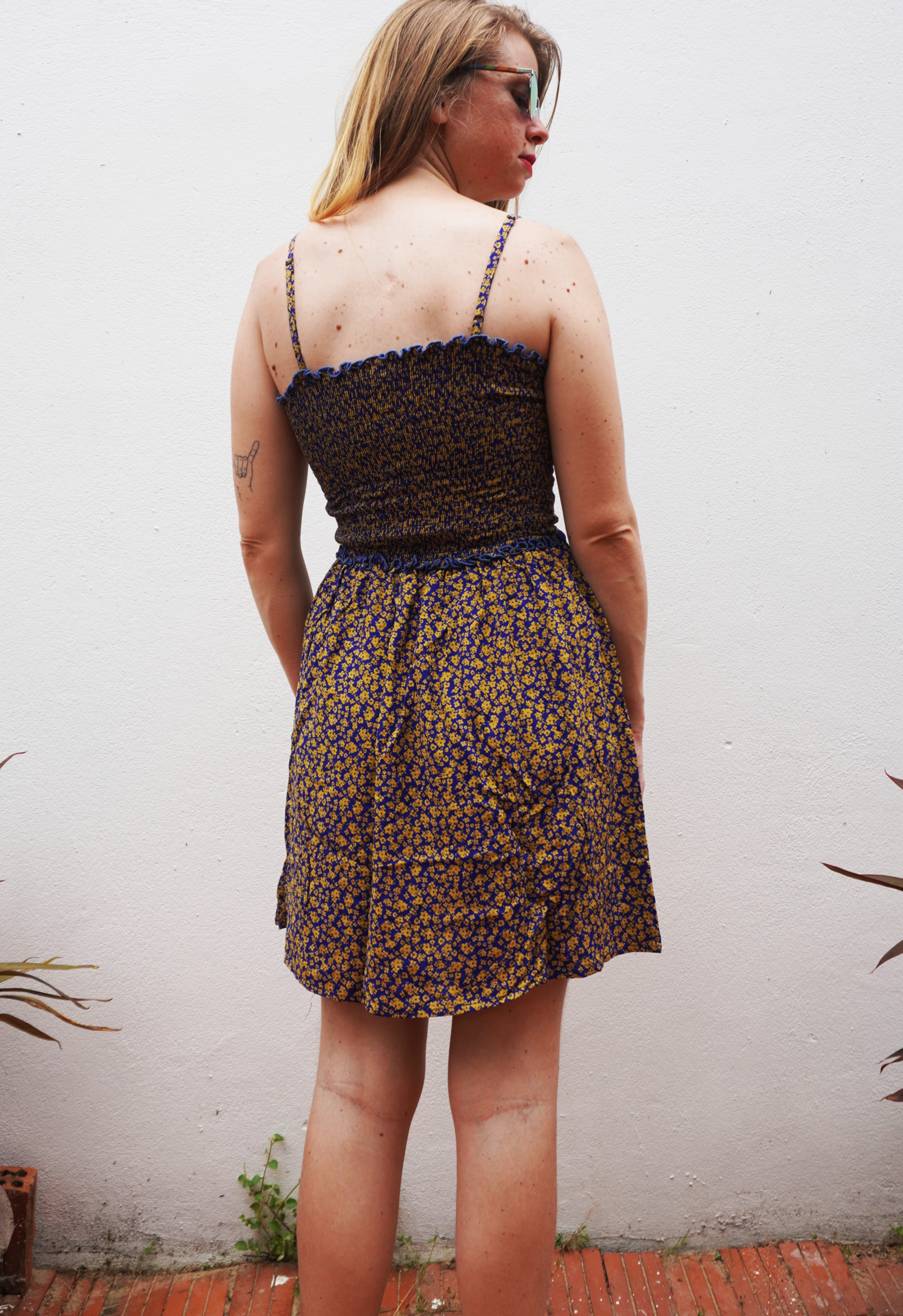 Woman wearing a purple and yellow floral dress against a white wall.