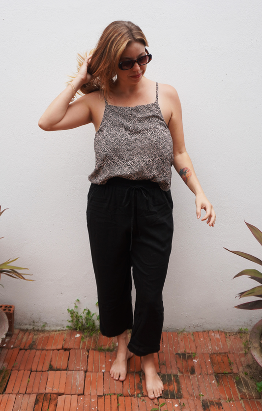 Woman wearing a gray tank top and black pants standing on a brick path with plants around.