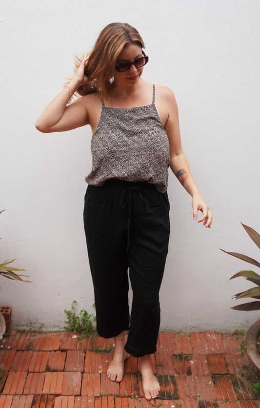 Woman wearing a gray tank top and black pants standing on a brick floor with plants around.