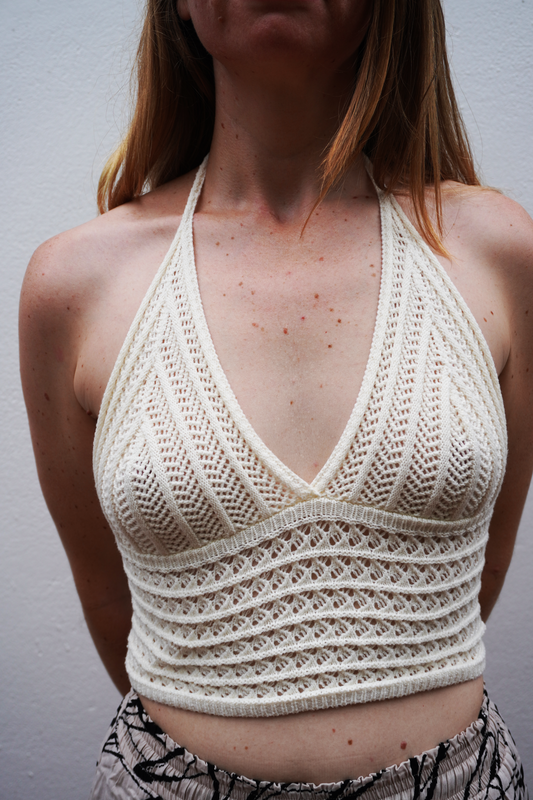 Woman wearing a beige knitted halter top against a plain background