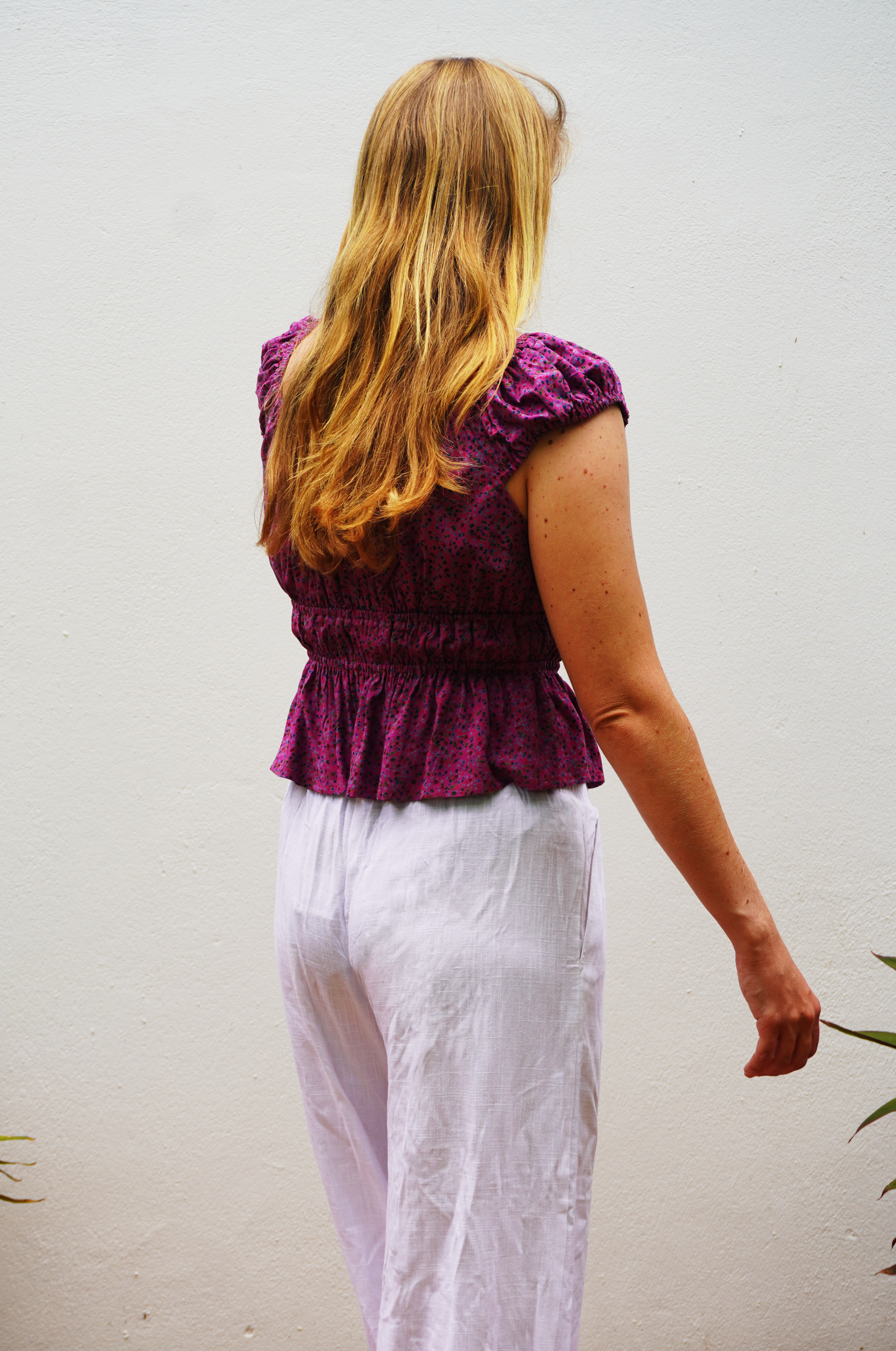 Person wearing a purple top and white pants against a plain background