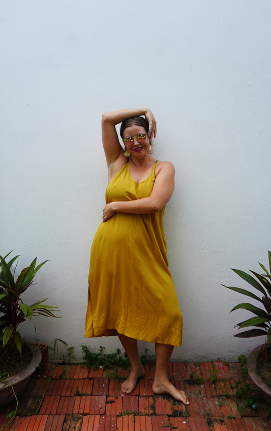 Woman in a yellow dress standing against a white wall with plants around.