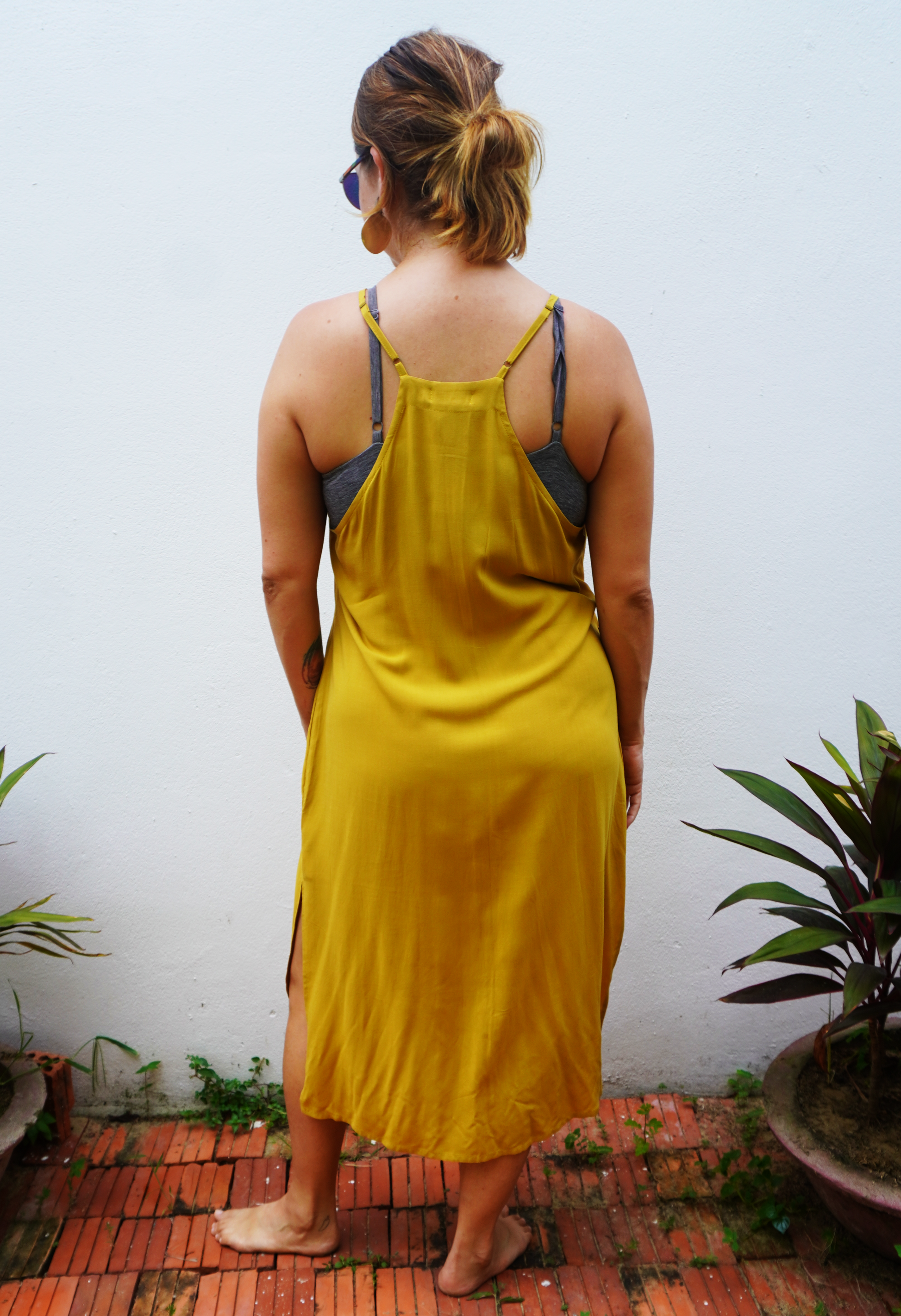 Person wearing a yellow dress standing in front of a white wall with plants around.