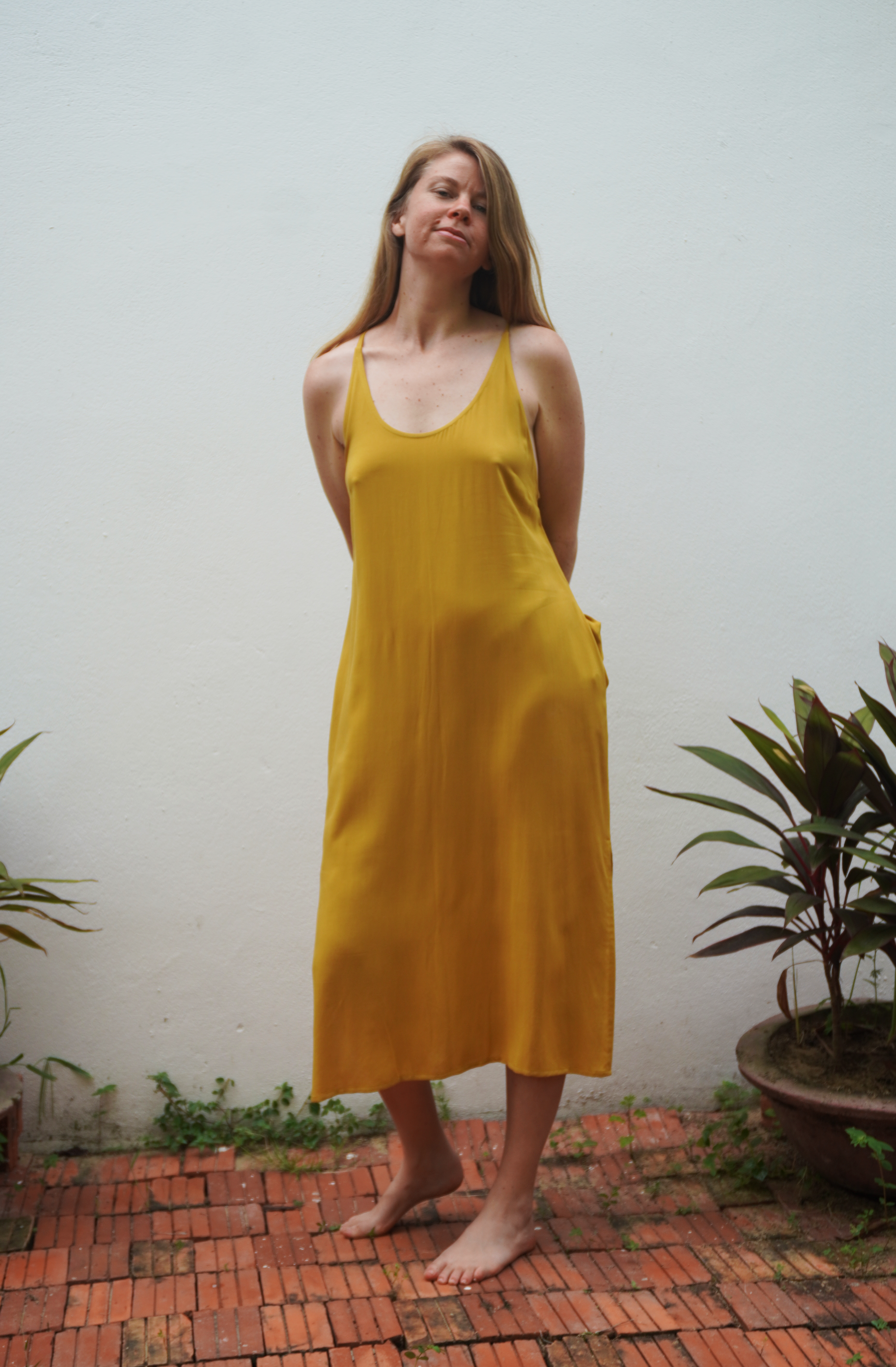 Woman wearing a yellow dress standing outdoors with plants in the background