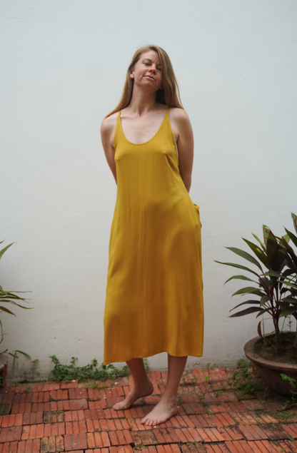 Woman wearing a yellow dress standing outdoors with plants in the background