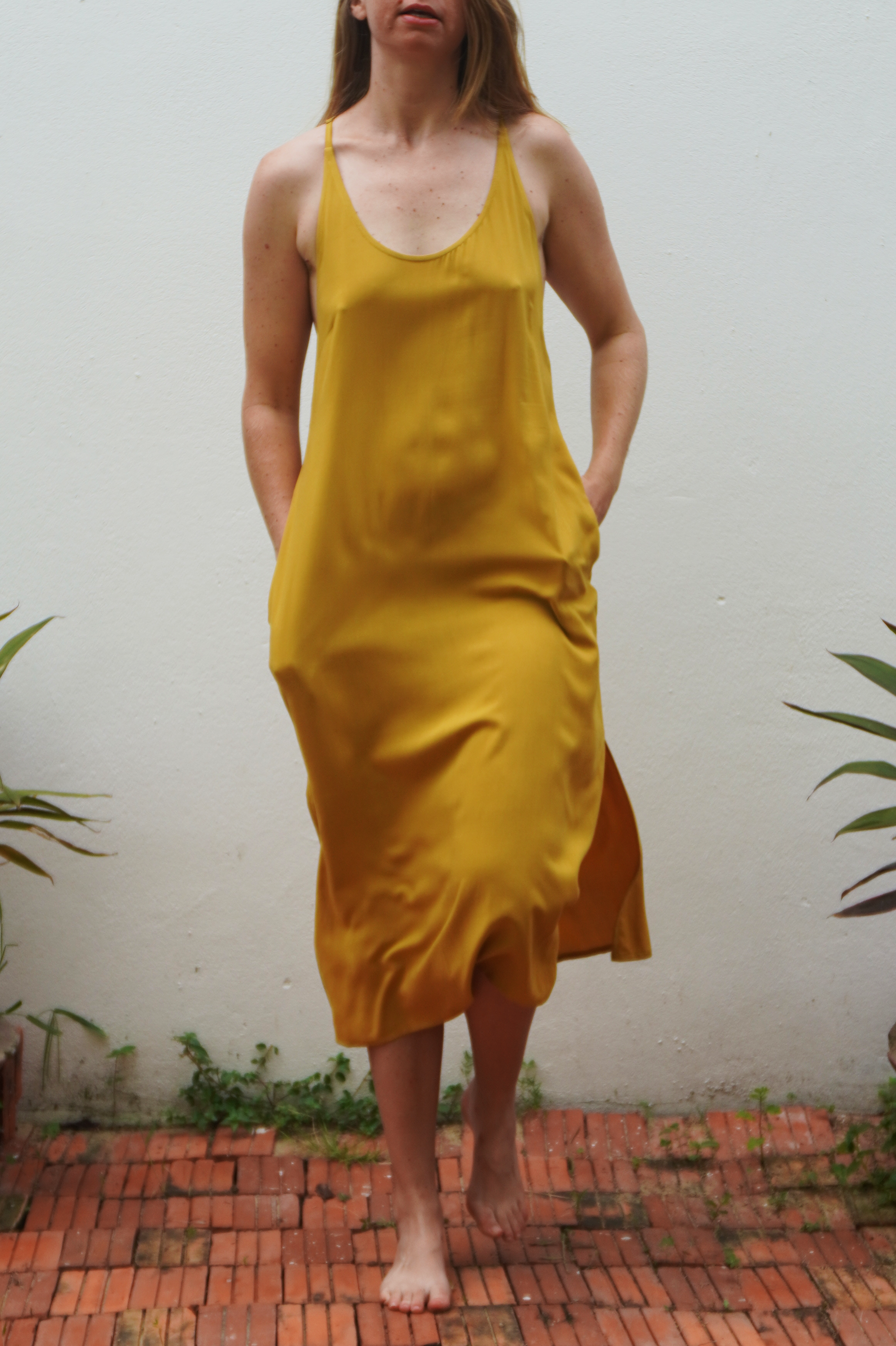 Person wearing a yellow dress standing on a brick path with plants around.